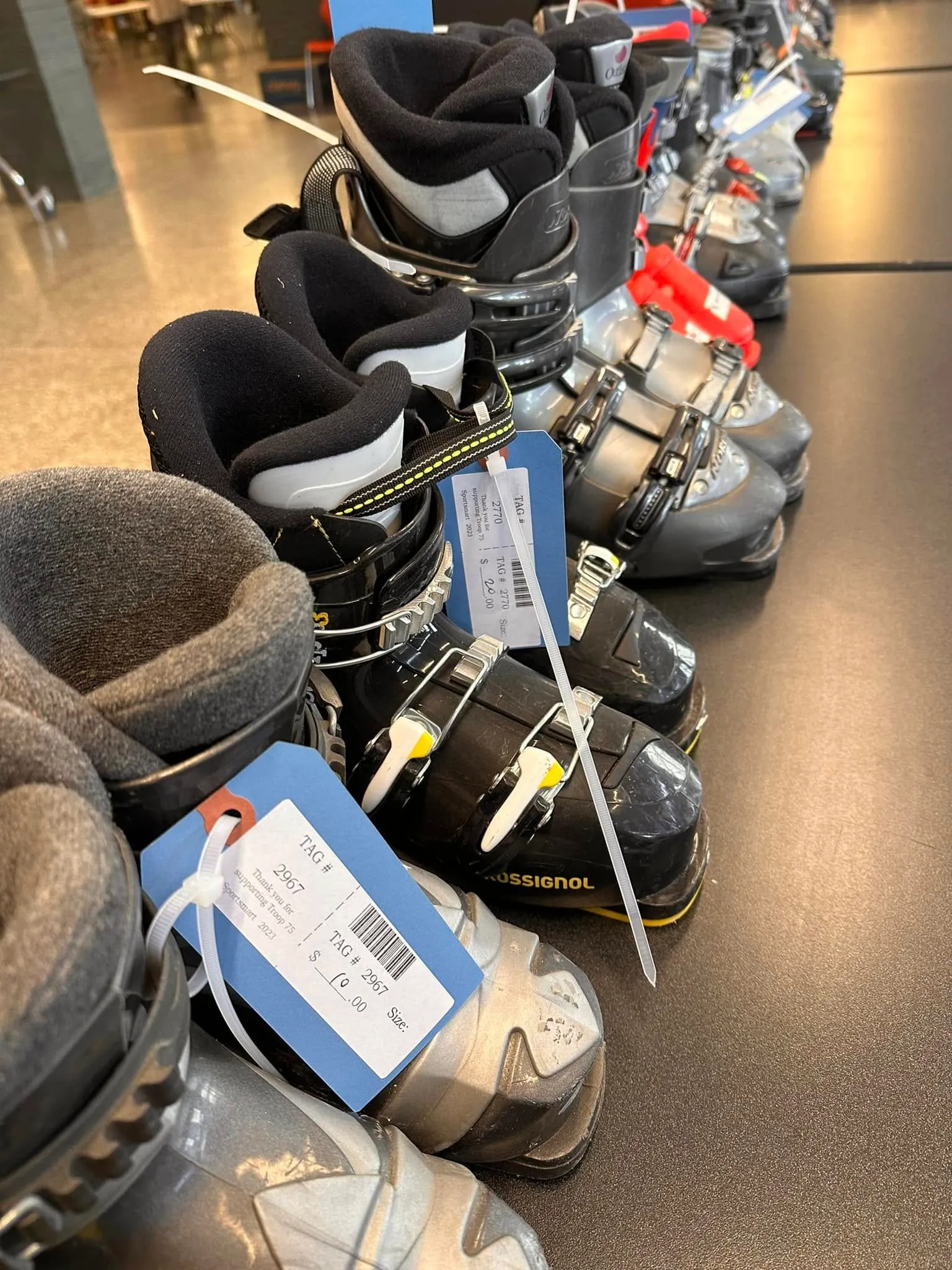 Ski boots on a sale table, each with a Sportsmart tag and barcode